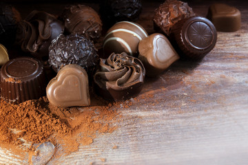 Fine chocolate pralines on cocoa powder as a love gift, corner background on rustic wood