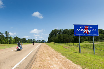 Two motorcycles passing by the Mississippi State welcome sign along the US Highway 61 in the USA;...