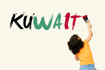 Cute little girl writing KUWAIT using painting brush on wall background