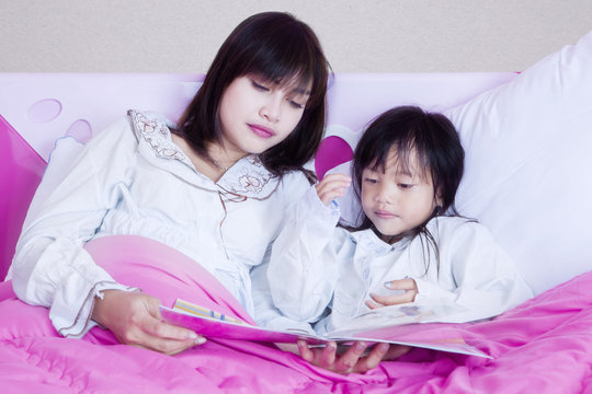 Pretty mother and girl read book on bed