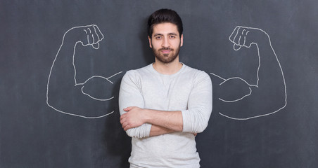 Young man against the background of depicted muscles on chalkboard