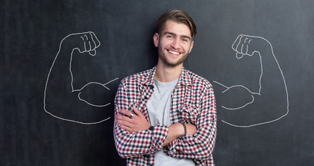 Young man against the background of depicted muscles on chalkboard