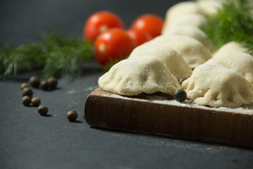 dumplings on a black background with fresh herbs and vegetables. homemade food. Traditional Russian food is pelmeni.