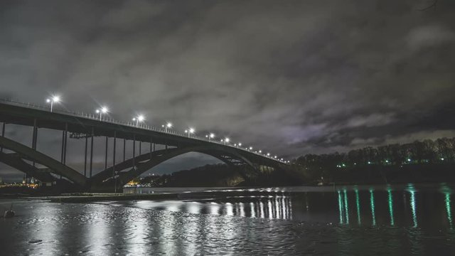 Time Lapse Tilt of arch bridge and river at night. Fast moving clouds and ice in the water