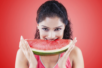 Young woman biting watermelon on red background