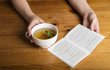 Woman hands with cup of tea and book