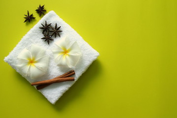 Fototapeta na wymiar White towel with flowers of plumeria with stars of anise and cinnamon sticks on the yellow background for spa theme.