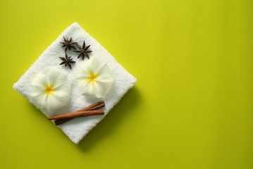 White towel with flowers of plumeria with stars of anise and cinnamon sticks on the yellow background for spa theme.
