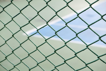 Fototapeta premium Closeup view of a fence with a blurred tennis court background.