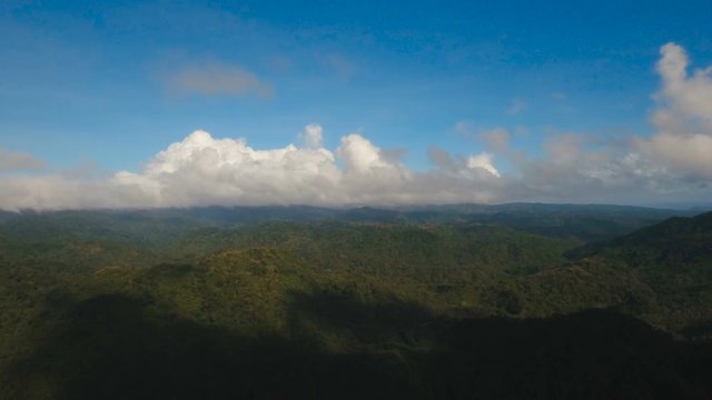 Aerial view: Mountains with rainforest covered with green vegetation and trees on the tropical island, landscape. Flying over mountains and hills with wild forest, sky clouds. Hillside rainforest and