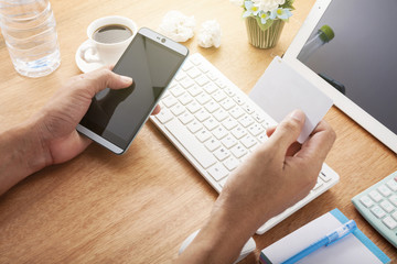 hand use smartphone with hand holding credit card on wood desk at home office, concept online payments shopping