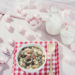 Breakfast set. mix oat granola in white bowl with pink heart sweet marshmallow on table set background, serve with white milk in glass and Bottle, top view, Healthy food concept, pastel tone color