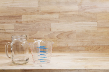 glass bottle and empty measuring cup on wooden background.