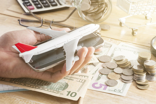 airplane model on smartphone in hand, money banknote,coins and Office desk wood table of Business workplace and business objects.
