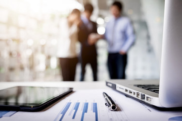 Close-up of business document in touchpad lying on the desk, office workers interacting in the background
