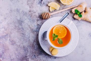 White cup of ginger tea with lemon, honey and mint on gray table background. Heathy concept. Top view with copy space