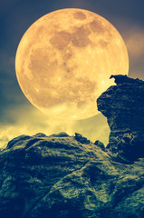 Boulder against sky with clouds and beautiful super moon at night. Outdoors. Sepia tone.