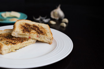 Grilled cheese sandwich on a white plate with butter, parsley, and garlic in the background
