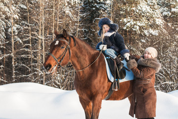 Fototapeta na wymiar Small girl and mom near horse in a winter
