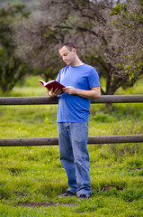 Reading outside in nature alone leaning against a wooden fence. Enjoying a leisure activity. 