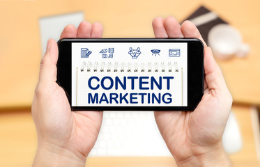 Watching two hand holding mobile phone with Content marketing word on screen and blur desk office background,Digital content concept