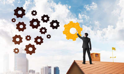 Businessman standing with back on house brick roof and drawing. Mixed media