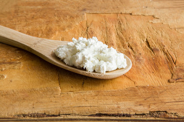 Cottage cheese in the wooden spoon on the old wooden board in the kitchen. Tasty, sweet meal with cinnamon and apricots. Healthy eating and lifestyle.