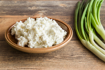 Cottage cheese in the dish on the wooden table in the kitchen. Healthy eating and lifestyle.