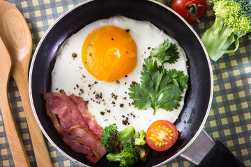 Breakfast with fried egg and bacon in dark pan on the table