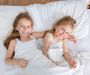 two little lovely sisters in white bed