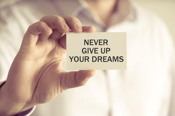Businessman holding NEVER GIVE UP YOUR DREAMS card
