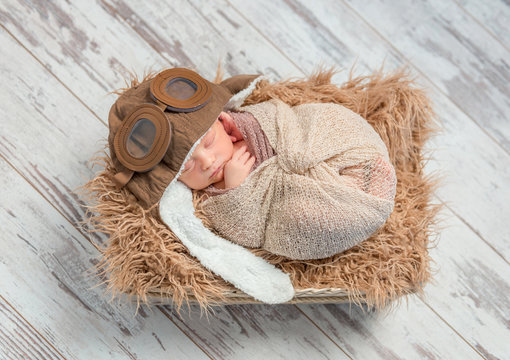 funny sleeping wrapped newborn with pilot hat, top view
