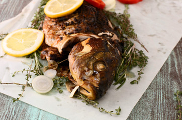 fried carp (fish) on  a paper for baking with lemon, onion and herbs (rosemary, thyme)