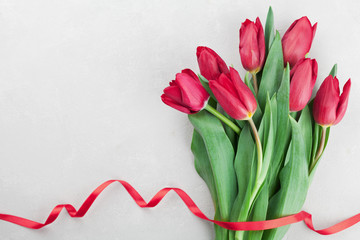 Spring tulip flowers with ribbon on light background top view in flat lay style. Greeting for Birthday, Womans or Mothers Day.