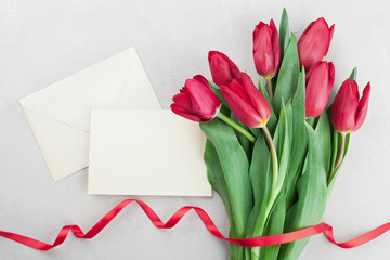 Spring tulip flowers with ribbon and paper card on gray stone table top view in flat lay style. Greeting for Birthday, Womans or Mothers Day.