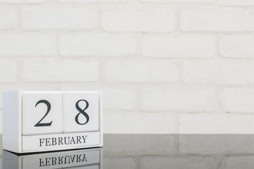 Closeup white wooden calendar with black 28 february word on black glass table and white brick wall textured background with copy space in selective focus at the calendar