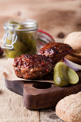 Cooked beef burger, buns and pickles on wooden table