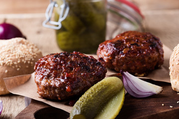 Cooked beef burger, buns and pickles on wooden table