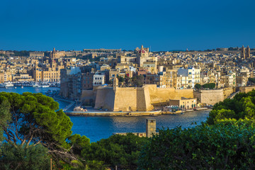 Fototapeta na wymiar Valletta, Malta - The view from Valletta with trees, Island of Senglea, Gardjola Gardens with watchtower, the Grand Harbour with boats and ships and clear blue sky