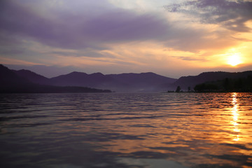 Sunset in the mountains of Altai. Dramatic sky, lake Teletskoe. The sunrise in the landscape of forest and pond. Purple fog over lake. Stunning views of nature. Twilight in mountains in a wooded area.