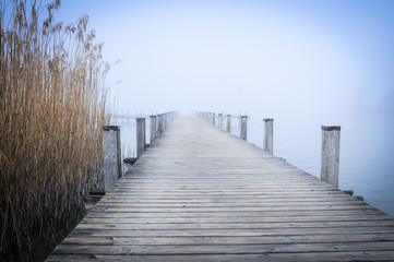 Ein einsamer Bootssteg am See im Winter mit Nebel