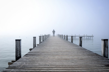 Obraz premium Mann auf Holzsteg im Nebel am Wasser
