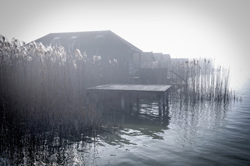 Bootshaus und Holzstege im Nebel am Seeufer