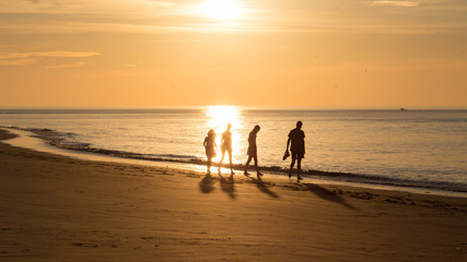 People walking on the beach at sunset during a warm summer evening