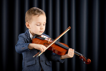 Little boy playing violin on dark curtain background