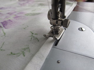 Close up detail of a sewing machine needle and the hemmed edge of white fabric