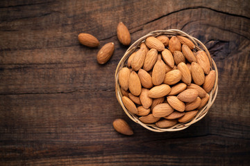 Almonds in willow bowl against dark rustic wooden background. Overhead view