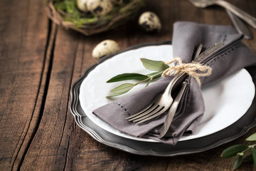 Easter table setting with vintage silverware with an olive branch on a white plate with quail eggs in a decorative nest at the background. With copy space for your text - Powered by Adobe