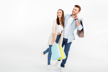 Happy young couple with shopping bags embracing and looking away on white