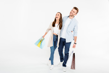 Happy young couple with shopping bags embracing and looking away on white